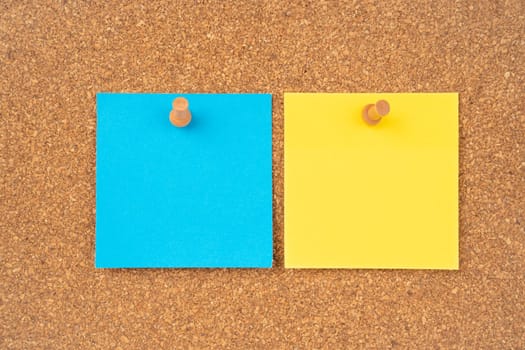 Blank yellow and blue color sticky note paper and wooden thumbtack on wooden background.