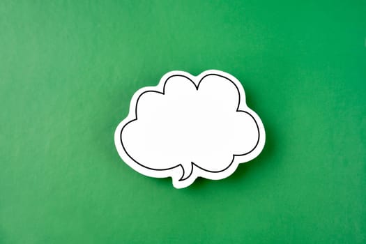 White speech bubble shaped post it note on green background with copy space.