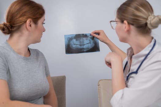 A woman doctor and a patient at the reception are discussing an x-ray of the jaw