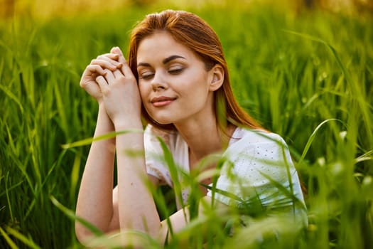 portrait of a woman sitting in the grass with her hands folded to her head. High quality photo