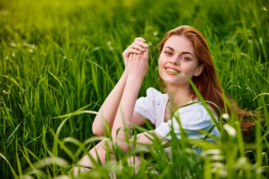 adorable, smiling woman sitting in nature relaxing in tall grass looking at camera. High quality photo