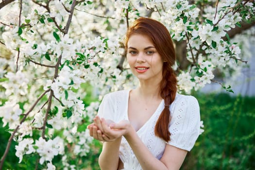 portrait of a beautiful red-haired woman against the background of a flowering tree with flowers in her palms. High quality photo