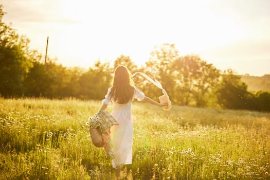 a woman in a light dress stands in a field in the warm rays of the setting sun holding a hat over her head. High quality photo