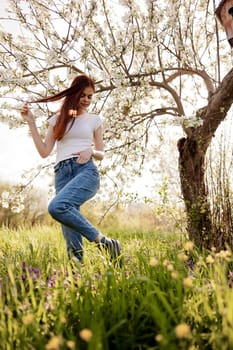 cheerful woman in casual clothes walks in nature near a flowering tree. High quality photo