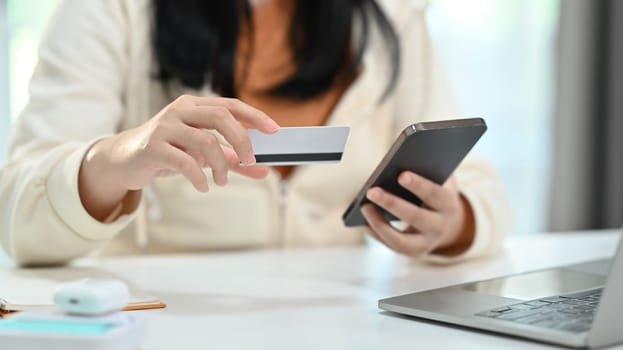 Cropped shot of young woman hand holding credit card and smartphone, paying online, entering information, shopping online.