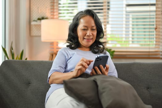 Smiling senior woman in casual clothes using smart phone, browsing wireless internet or chatting online.