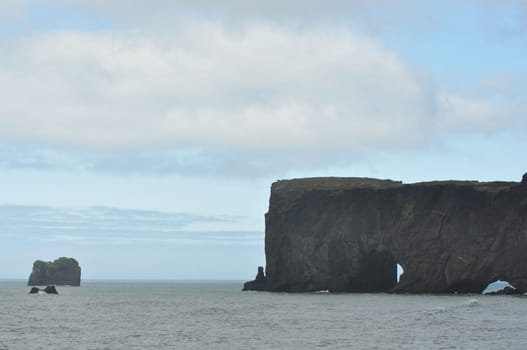 Scenic view of Icelandic peninsula with waves hitting huge black rocks at overcast Dyrholaey Cape