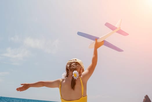 Kid playing with toy airplane. Children dream of travel by plane. Happy child girl has fun in summer vacation by sea and mountains. Outdoors activities at background of blue sky. Lifestyle moment