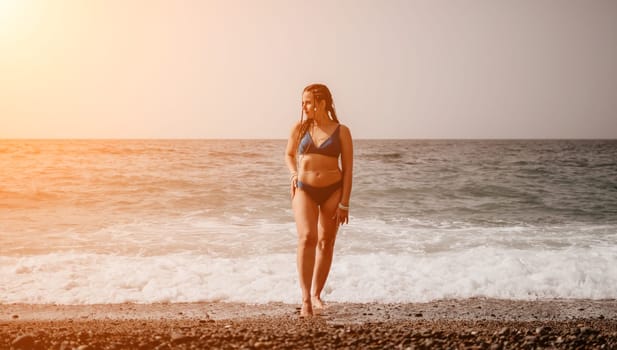 Beach vacation. Hot beautiful woman in sunhat and bikini standing with her arms raised to her head enjoying looking view of beach ocean on hot summer day.