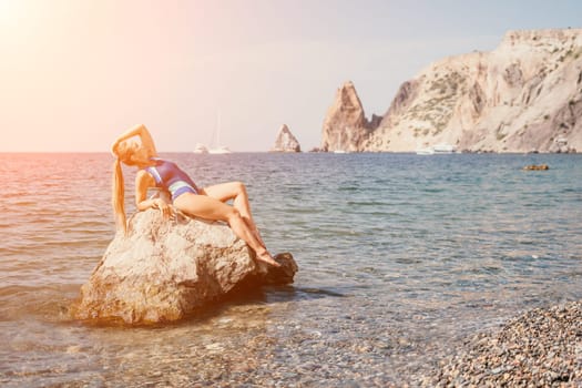 Woman travel sea. Young Happy woman in a long red dress posing on a beach near the sea on background of volcanic rocks, like in Iceland, sharing travel adventure journey