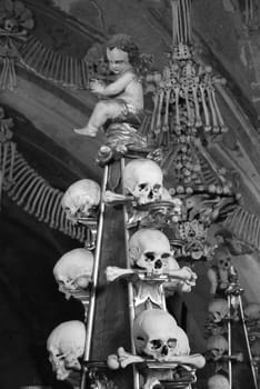 Grayscale shot of an angel sculpture on a stack of skulls in the Sedlec Ossuary in Kutna Hora