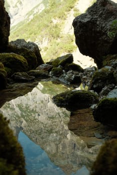 The Leogang mountains are reflected in the crystal clear water of the spring at the Birnbachloch near Leogang, Austria