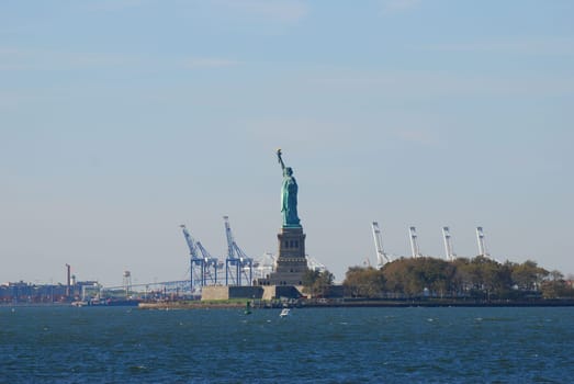 Statue of Liberty and Liberty Island with cranes in background in New York, USA