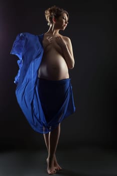 Pretty pregnant woman posing with flying cloth in studio