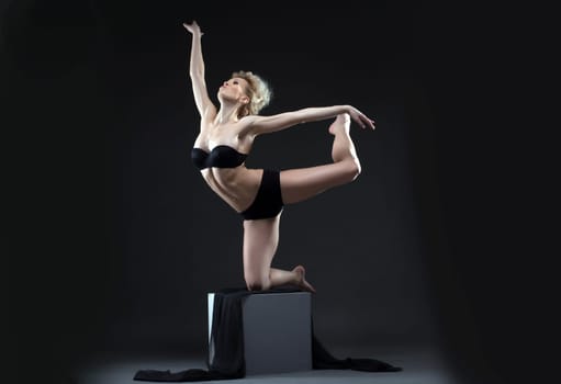 Image of seductive young dancer balancing on cube in studio