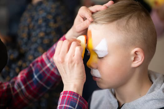 Makeup artist draws face painting on the face of a little boy.