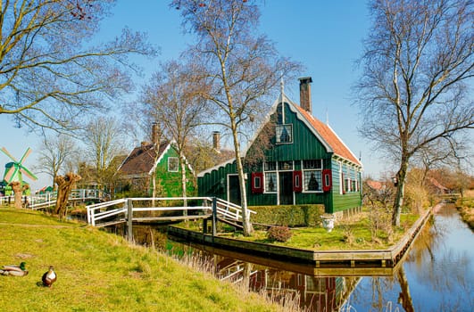 Typical Dutch scenery with a historic home on a lake and an antique windmill in the background
