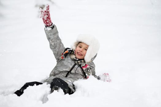 A joyful boy in warm clothes lies in the snow. Child on a winter walk.