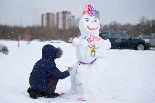 A boy paints a snowman on a winter day.