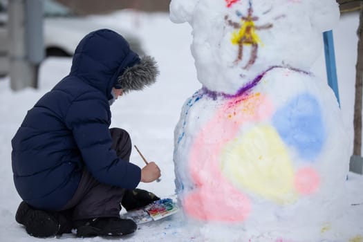 A boy paints a snowman on a winter day.