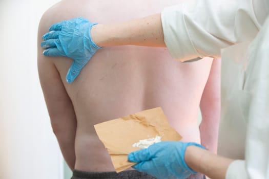 A nurse smears a body covered with an allergic rash to a patient.The hands of a doctor smear a person's skin with a white ointment.