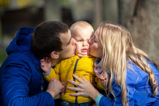 Happy family mom dad and little son. A woman and a man kiss a small child.