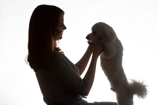 Dark silhouette of a girl with a bichon puppy on a white background.