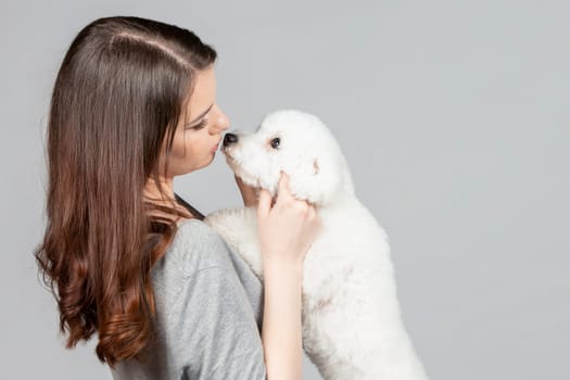 A beautiful young woman kisses and hugs her bichon puppy. Love between owner and dog.