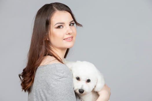 A beautiful young woman is holding her bichon puppy. Love between owner and dog. The girl is playing with the dog.