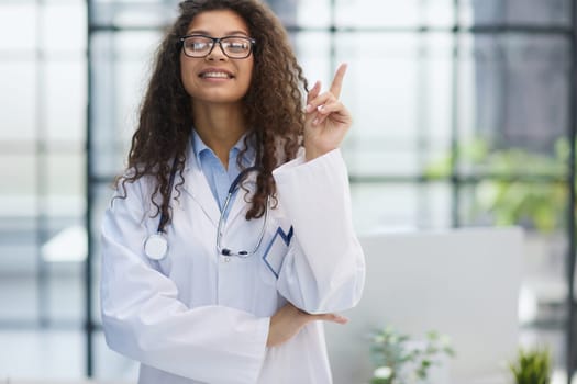 Portrait of an attractive young female doctor in a white coat points her finger
