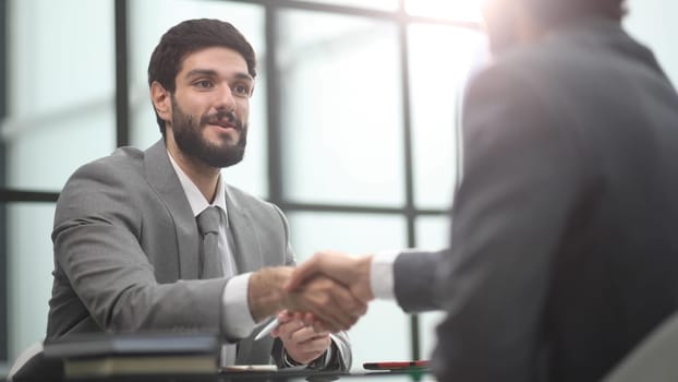 sitting at table wile advisor and investor shaking hands over table in office