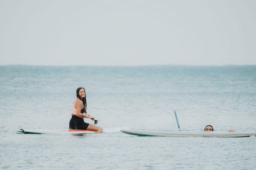 Sea woman and man on sup. Silhouette of happy young woman and man, surfing on SUP board, confident paddling through water surface. Idyllic sunset. Active lifestyle at sea or river