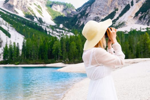 Blonde hair female photographer in straw hat and white dress taking pictures of Dolomites near Lake Braies with copy space