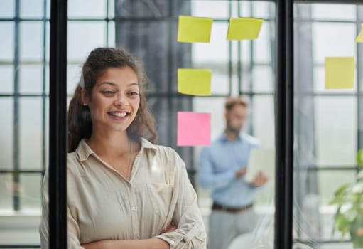 Bringing her vision to life. Shot of a confident businesswoman presenting an idea to her colleague using adhesive notes on a glass wall in the office.