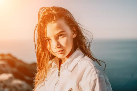 Brown-haired young romantic teenager girl corrects long hair on beach at summer evening wind