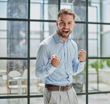 Portrait of a young businessman in a blue shirt shaking his fists celebrating his success in the office