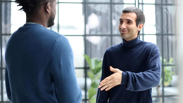 Diverse male colleagues in modern office corridor, young african american and caucasian business people discussing common project work, meeting in company work