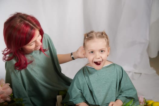 Amazing pretty mother and daughter having fun with flowers in 8 March or in Mother's day. Red haired mom and small little blonde girl having lovely free time on white background in studio