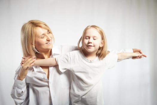 Portrait of blonde mother and daughter who having communicate and play on a white background. Mom and little girl models pose in the studio. The concept of love, friendship, caring in the family