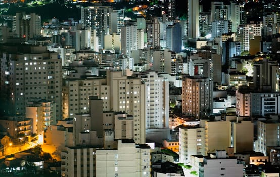 Long-distance compressed perspective of Juiz de Fora at night, showcasing the central urban skyline with its brightly-lit skyscrapers and bustling city life.