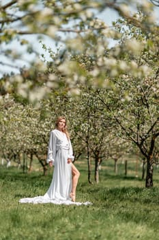 Blond blooming garden. A woman in a white dress walks through a blossoming cherry orchard. Long dress flies to the sides