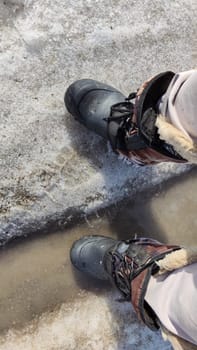 Feet of Hunter or fisherman in big warm boots on winter day on snow. Top view. Fisherman on the ice of a river, lake, reservoir on spring day with melting ice. Dangerous fishing in autumn