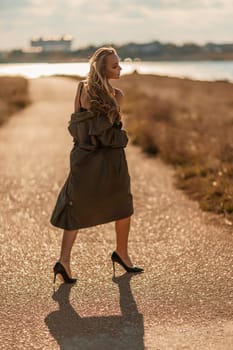 Portrait blonde sea cape. A calm young blonde in an unbuttoned khaki raincoat walks along the seashore, under a raincoat a black skirt and top.