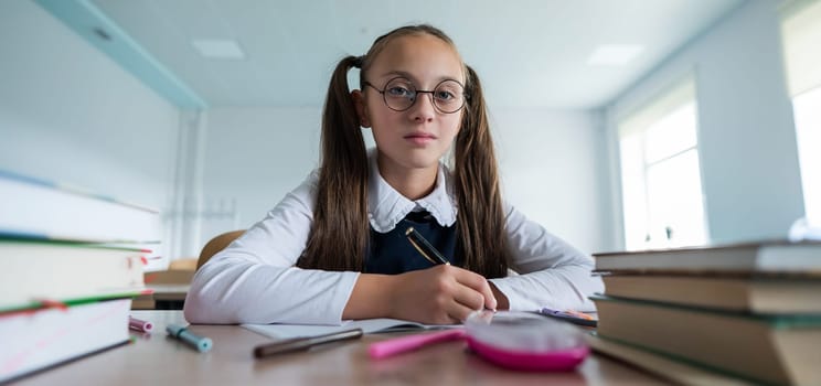 Caucasian girl with two ponytails sits at her desk and writes in a workbook