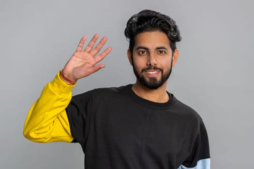 Come here, join us. Welcome. Hindu bearded man showing inviting gesture with hands, ask to join, beckoning to coming, gesturing hello, goodbye. Handsome indian guy isolated on gray studio background