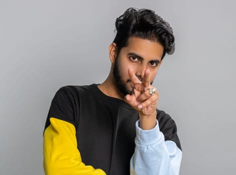 I am watching you. Young confident indian man pointing at his eyes and camera, show I am watching you gesture, spying on someone. Handsome bearded hindu guy isolated alone on gray studio background