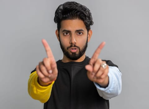 Indian handsome man shakes finger and saying No, be careful, scolding, giving advice to avoid danger mistake, disapproval sign. Young guy isolated alone on gray studio background. People lifestyle