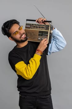 Indian man using retro tape record player to listen music, disco dancing of favorite track, having fun, entertaining, fan of vintage technologies. Handsome hindu guy isolated on gray background