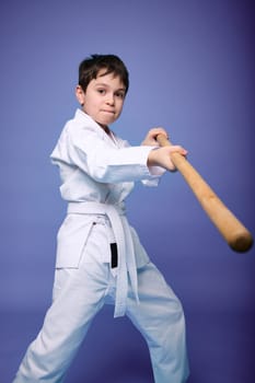 Confident strong concentrated Caucasian teenage boy - Aikido wrestler in white kimono practicing fighting skills with wooden jo weapon in his hands. Oriental martial arts practice concept. Copy space