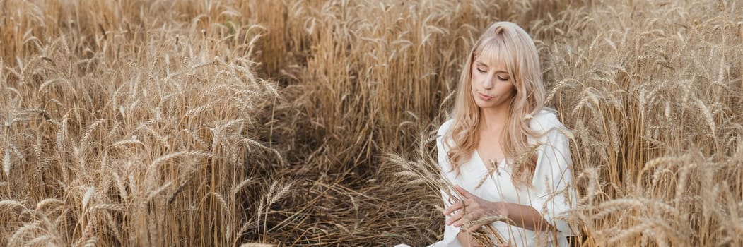 A blonde woman in a long white dress walks in a wheat field. The concept of a wedding and walking in nature.